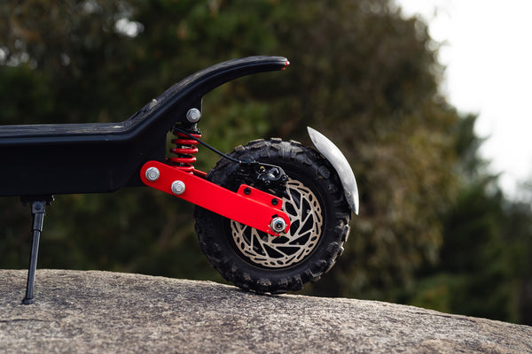 Close-up of a scooter wheel with red suspension fork on a blurred natural background