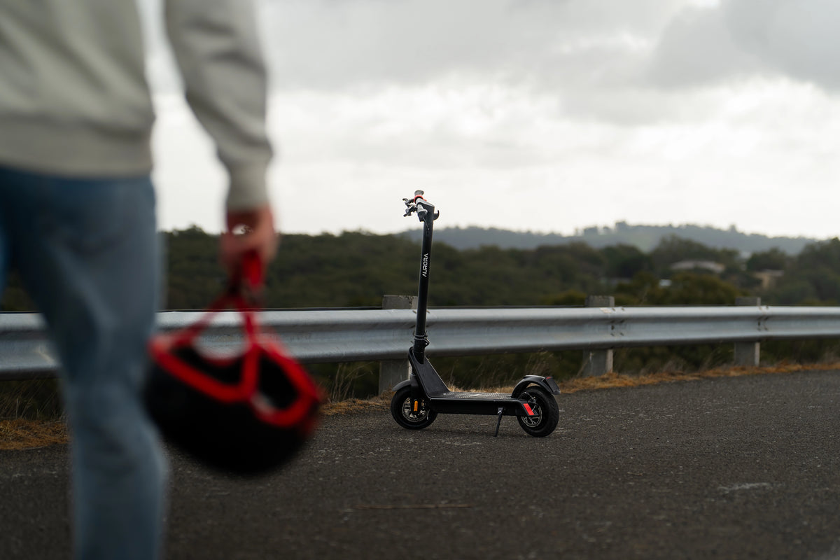 Person holding a helmet with an electric scooter on a road