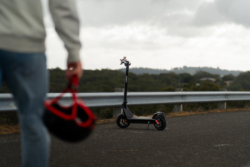 Person holding a helmet with an electric scooter on a road