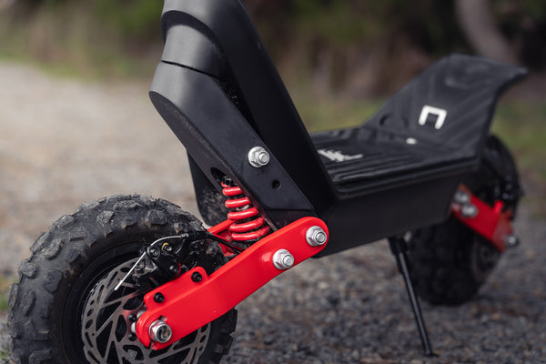 Close-up of a scooter's suspension system with red spring and black frame.