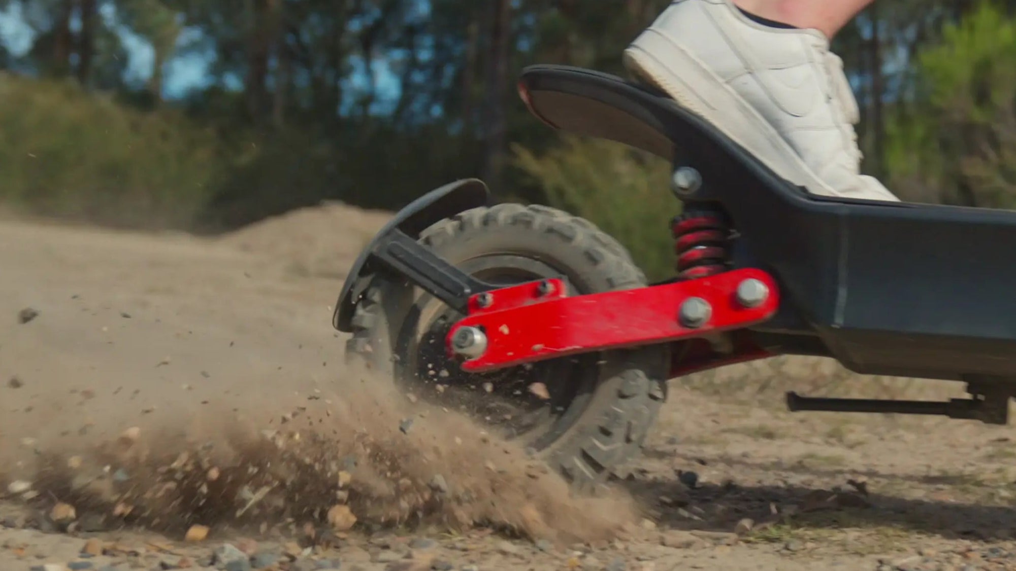 Person riding an electric scooter on a dirt path with trees in the background